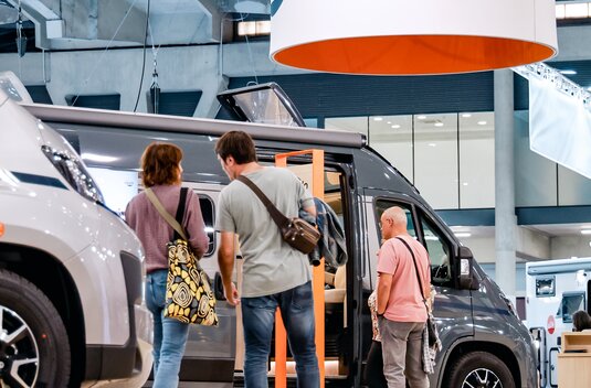 Visitors in front of a Carado motorhome at a trade fair, with the camper van open and the Carado logo above the stand