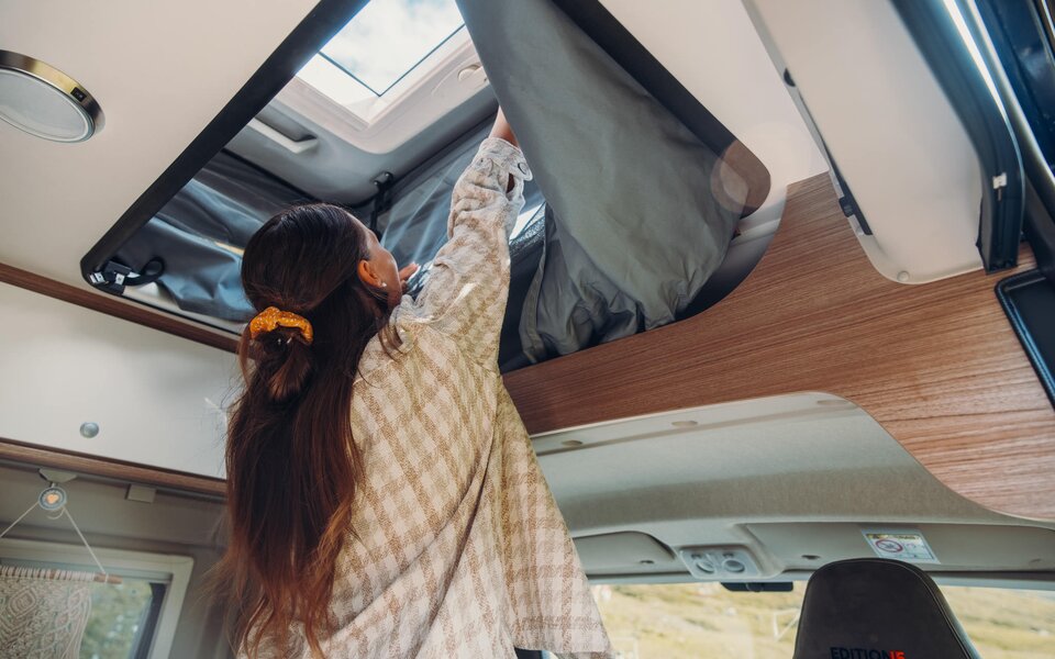 Une personne ouvre le lit de pavillon dans un camping-car Carado avec vue sur le lanterneau