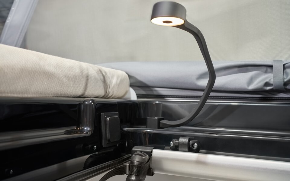 Lampe de lecture près du lit dans le camping-car Carado, gros plan sur le matelas et l’espace nuit