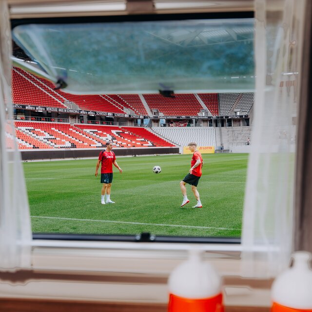 View from a Carado motorhome window onto a football pitch with two players in the stadium