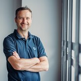 Mann im Carado Poloshirt mit verschränkten Armen am Fenster