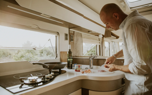 Man cuts onions in the kitchen of a mobile home - the pan is on the gas stove