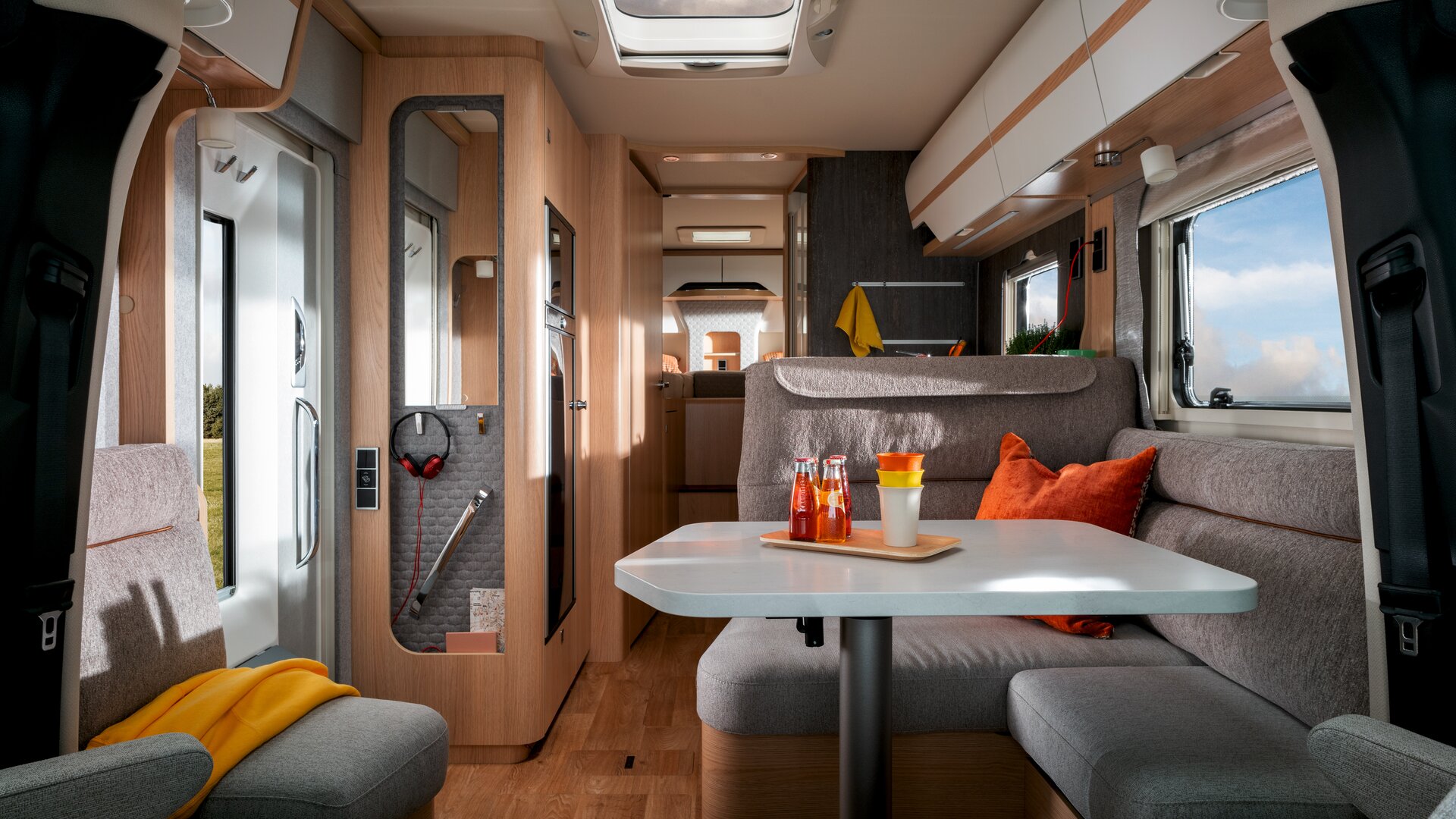 Dans le camping-car Mercedes Sprinter HYMER B-Klasse MasterLine T avec puits de lumière, il y a des boissons et des gobelets sur la table, le coin salon est rembourré en gris.