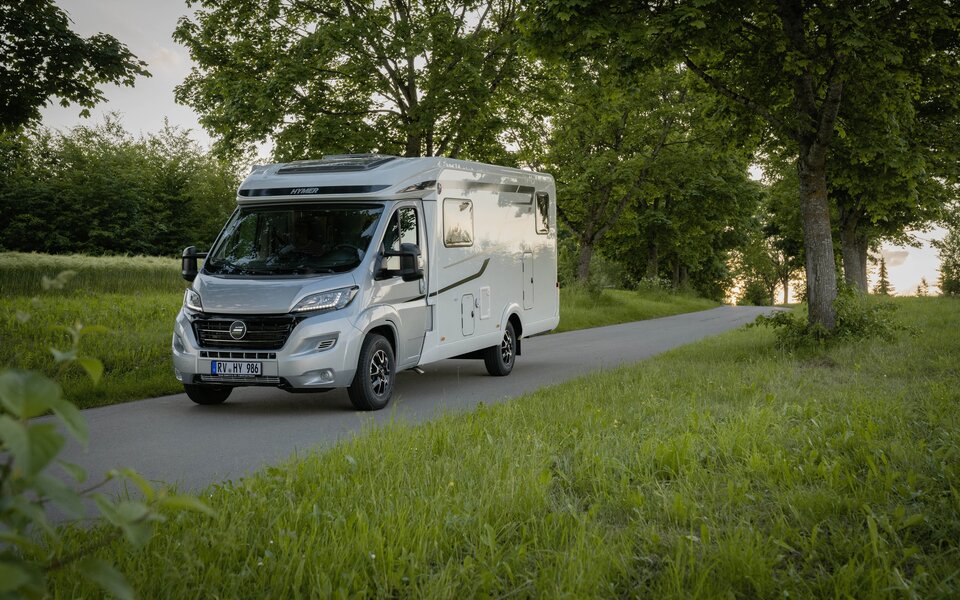 HYMER Exsis-t 580 on a narrow street amid trees and green meadows