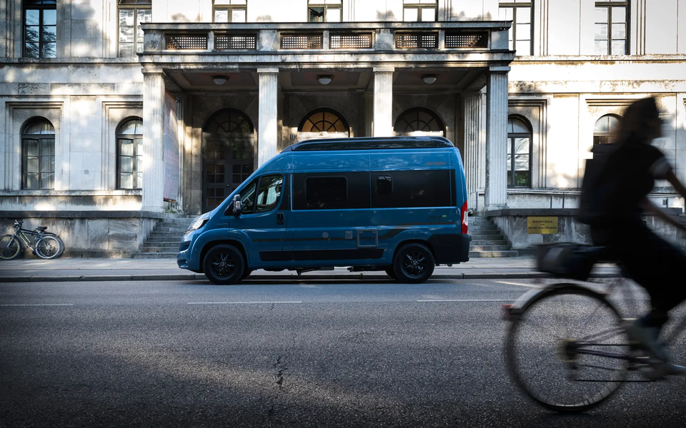 Blue metallic painted camper van HYMER Free is parked in front of an old building in the city