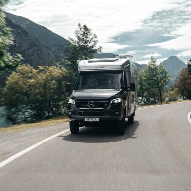 Le HYMER ML-T est vu de face, en train de virer dans un virage. L'environnement est flou en raison du mouvement.