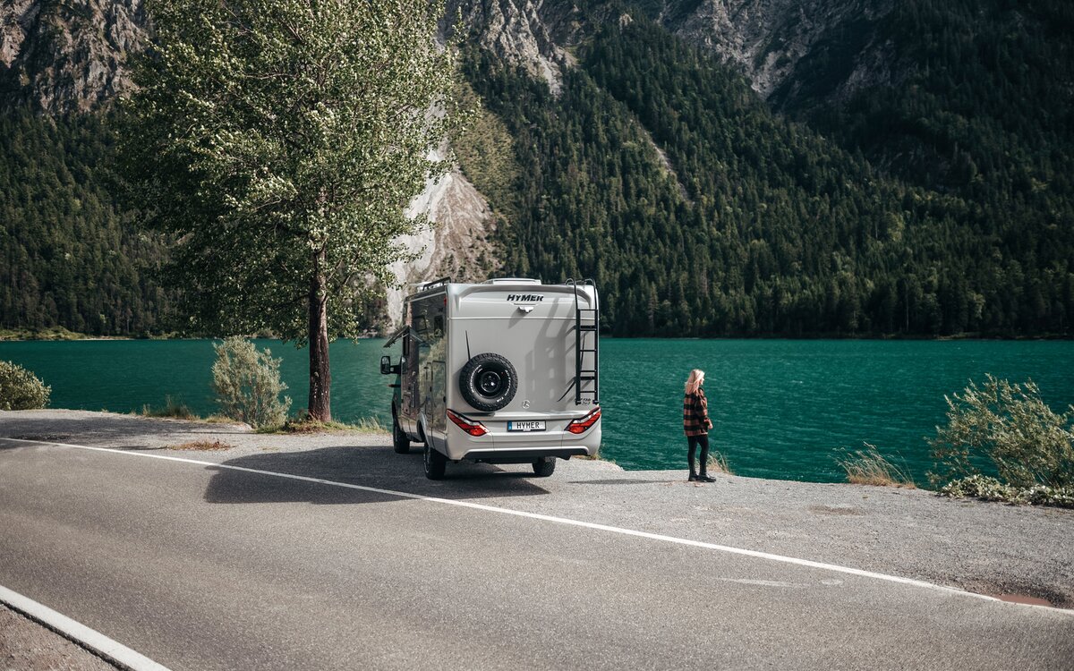 Une femme se tient devant l'arrière du HYMER ML-T et regarde un lac turquoise.