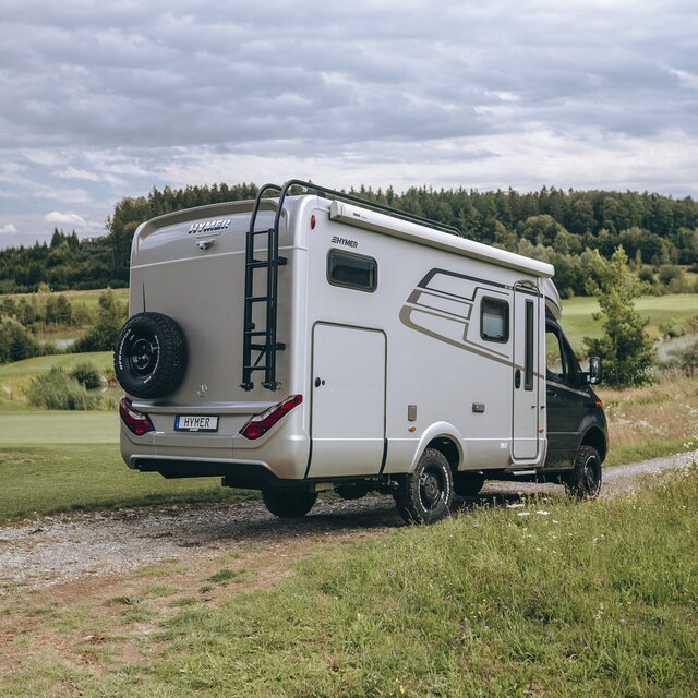 Le HYMER ML-T est vu de l'arrière, stationné sur un chemin entre deux prairies.