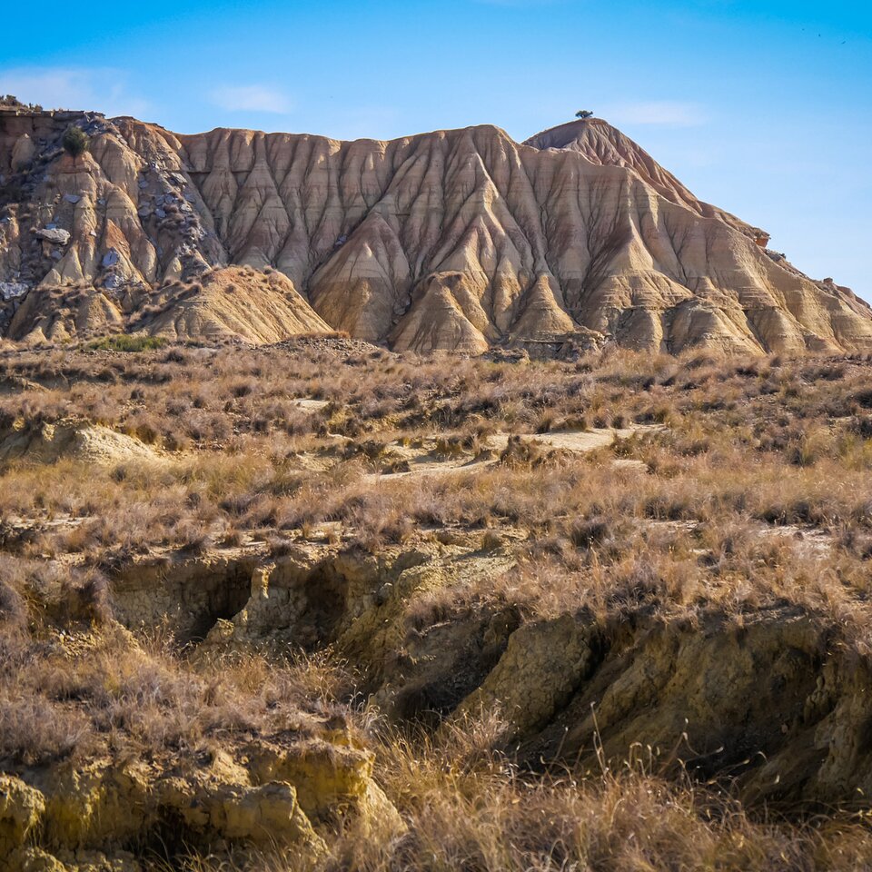Image shows landscape from a journey in a Mercedes campervan along the most beautiful routes through the Pyrenees with grasses, hills and barren ground.