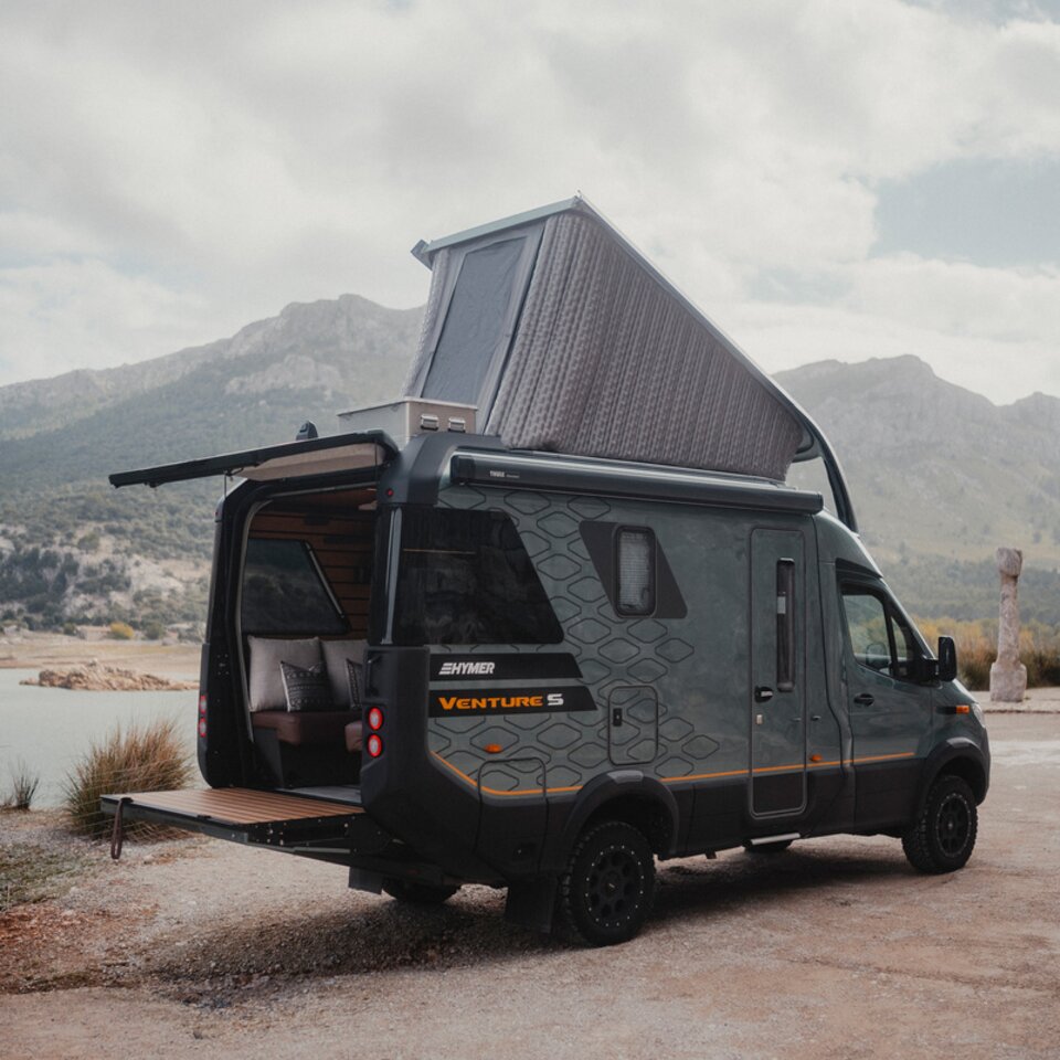 View from the rear side of the Venture S, with the pop-top and Sunset Deck extended, mountains and water in the background.