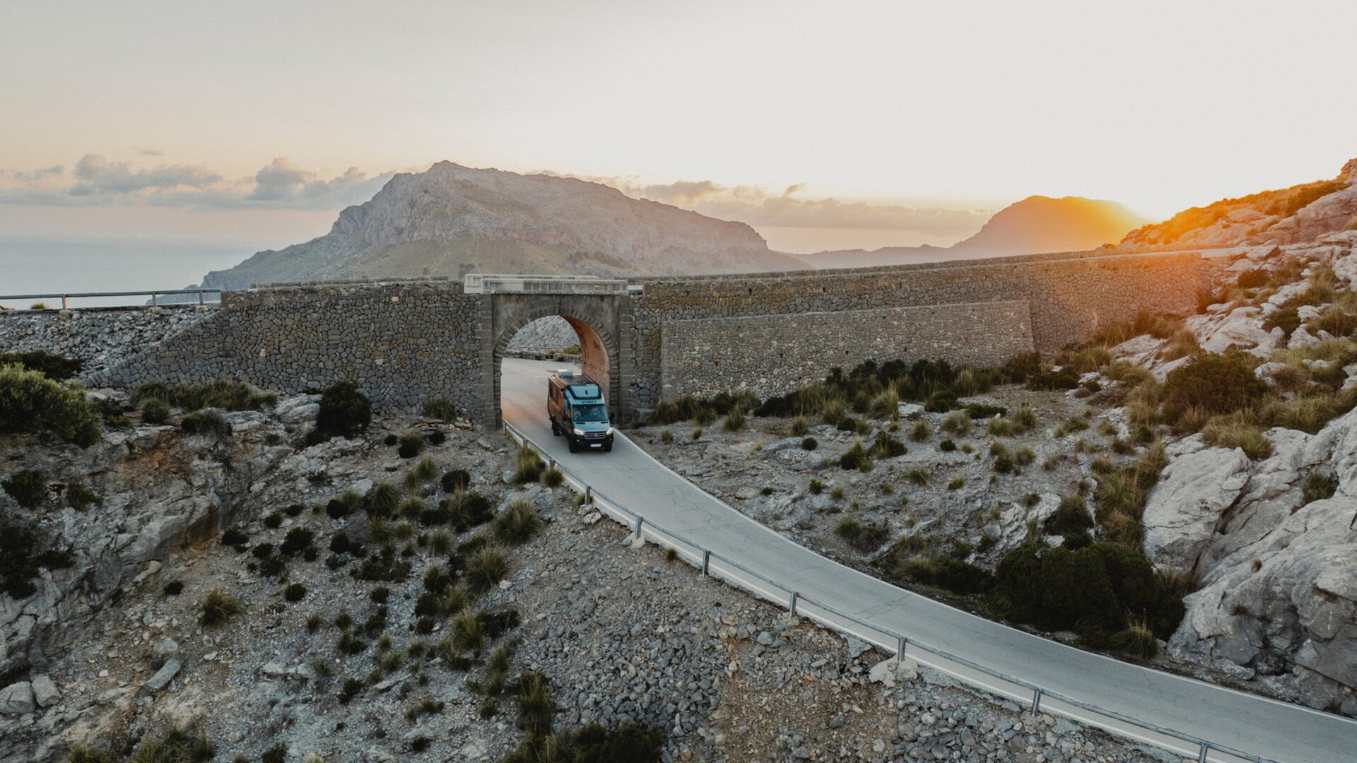 View from above the front of the Venture S, the vehicle is driving through an archway, with mountains and the sea in the background.