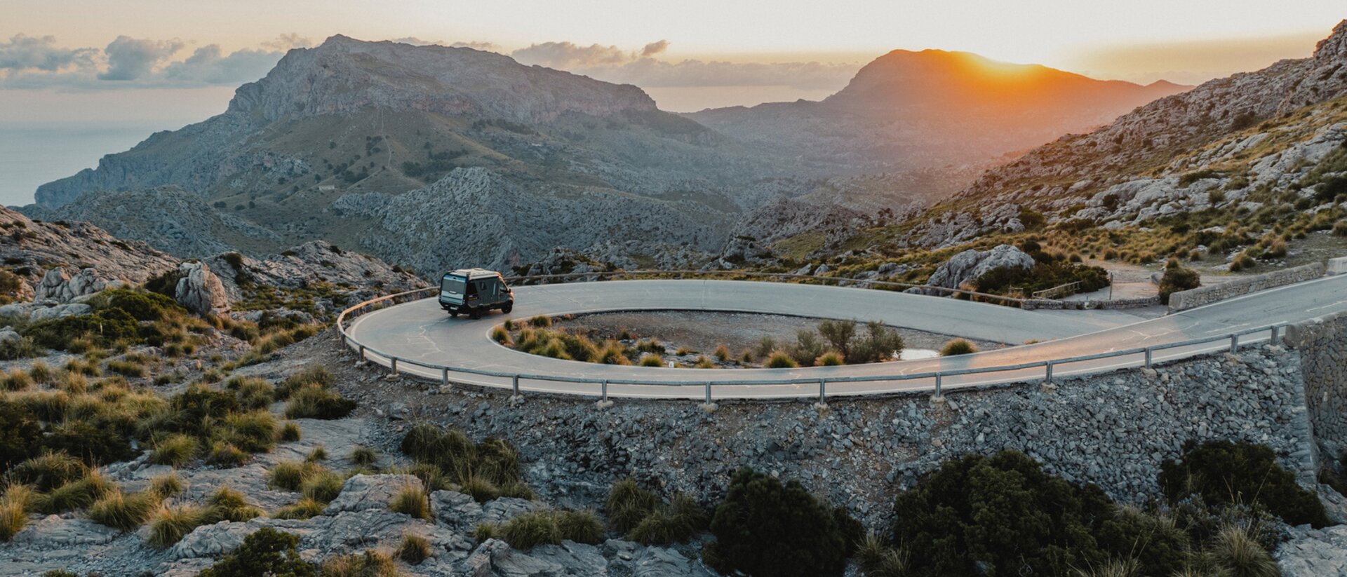 View from the rear of the Venture S, the vehicle is driving down winding roads, with mountains and the sea in the background.