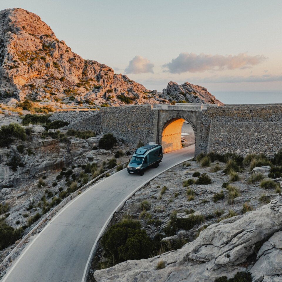View from above the front of the Venture S, the vehicle is driving through an archway, with mountains and the sea in the background.